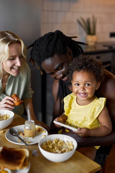 Boldog gyermek lány néz video rajzfilmek okostelefon, miközben étkezés a szülőkkel — Stock Fotó