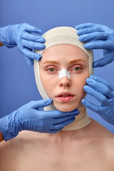 Chirurgien cultivé dans des gants scotchant le visage de la femme avec un bandage après une chirurgie plastique — Photo