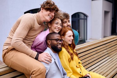 Happy diverse business people sit on bench outdoors smiling, looking at side, african and caucasian men and ladies in stylish clothes posing at camera, outside of office. business, people concept