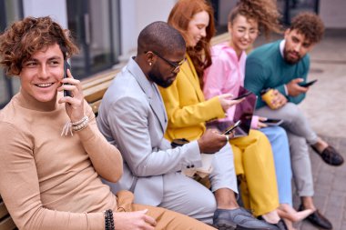 happy businesspeople walking, sitting on bench, using smartphones. young Caucasian and african colleagues chatting. focus on curly nice guy talking on phone. outside of office. business people