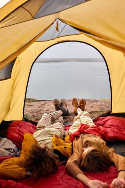 couple relaxing in camper tent and enjoying mountain autumn lake views. Cozy early autumn couple hiking traveling concept image. young caucasian relaxed man and woman having rest