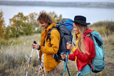 couple with bag pack on back holding hiking pole during hiking jurney, active athletic man and woman in colorful sportive outfit, vacation in nature outdoors. travel, sport, adventure concept