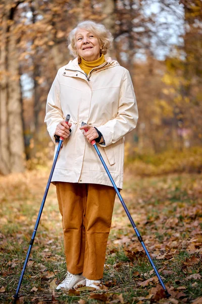 elderly woman lead healthy lifestyle, nordic walking in park.Senior active caucasian woman looks happy. Pretty aged senior woman having recreation in park. autumn season