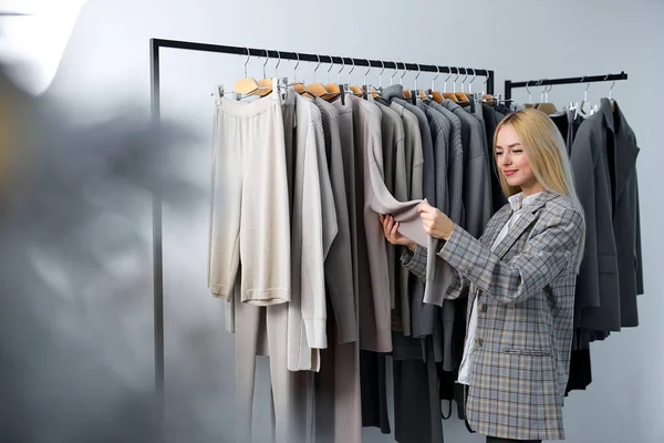 Woman looking at new collection of stylish clothes on hangers clothing rack rails, fashion design studio store concept. blonde caucasian female in jacket make choice, young customer woman