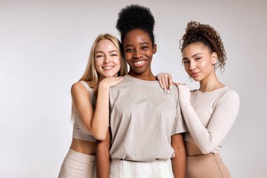 three smiling beautiful models are posing on white background. Close-up portrait of young women in casual outfit posing at camera together, looking happy, cheerful. copy space. black, caucasian