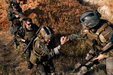 caucasian european men help each other during the military operation while climbing on mountain, one of them giving hand and helping to climb. Help, support, assistance in a dangerous situation