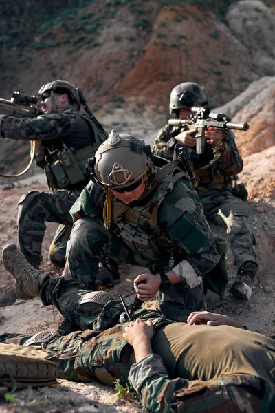 soldier saving life of injured comrade lying on ground, need medical help. outdoors in mountains. Private Military Contractor during the rescue operation. counter terrorism concept.