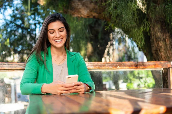 Mutlu üniversite öğrencisi gülümsüyor ve cep telefonunu parkta eğlenmek için kullanıyor.