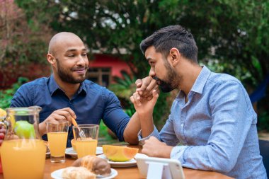 Romantik eşcinsel çift dışarıda kahvaltı yapıyor ve öpüşüyorlar.
