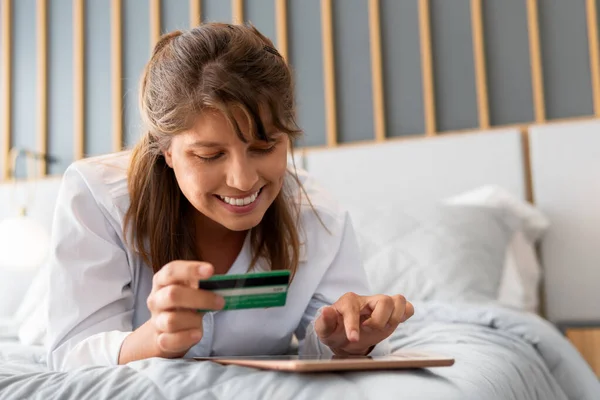 happy woman shopping online with credit card in the bedroom