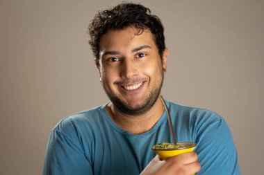 Portrait of a young man looking at the camera holding a mate chimarrao drink.