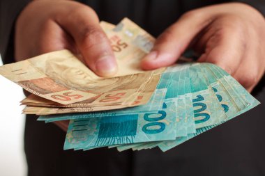 Adam Brezilya para birimini elinde tutuyor. Para, başarı ve ödeme konsepti.