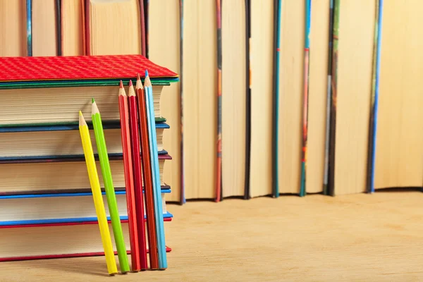 Pile of books and colored pencils on a wooden surface against th — Stock Photo, Image