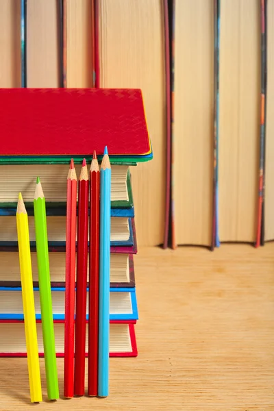 Stapel von Büchern und Buntstiften auf einer hölzernen Fläche gegen th lizenzfreie Stockbilder