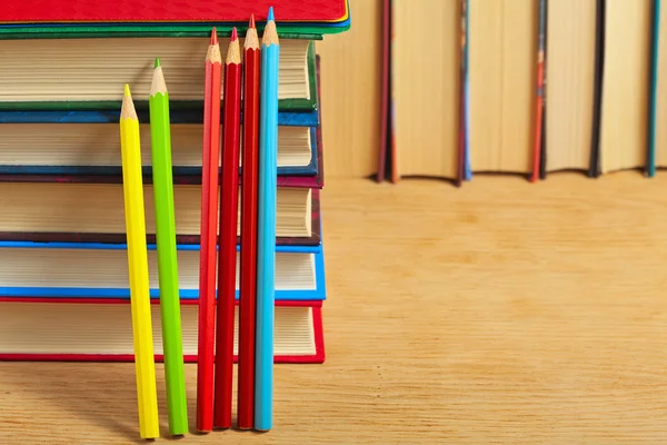 Pile of books and colored pencils on a wooden surface against th — Stock Photo, Image