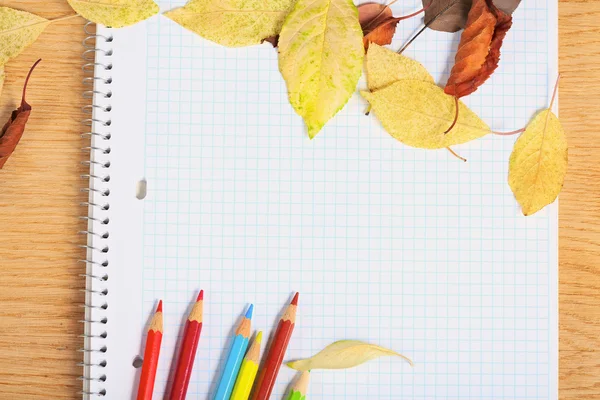 Cuaderno con lápices de colores y hojas de otoño sobre un oleaje de madera — Foto de Stock