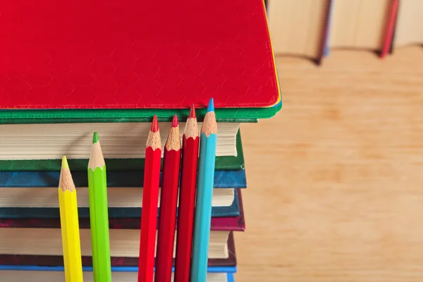 Stapel boeken en kleurpotloden op een houten ondergrond. Stockafbeelding