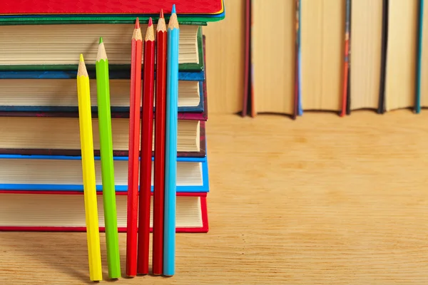 Stapel von Büchern und Buntstiften auf einer hölzernen Fläche gegen th Stockfoto