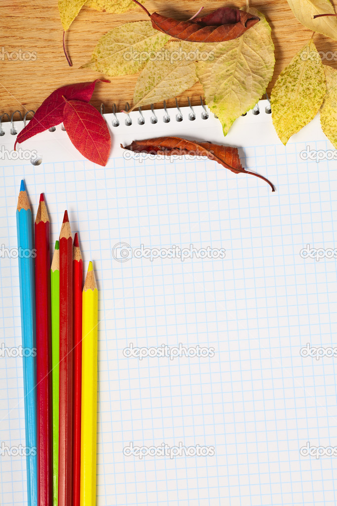 Notebook with colored pencils and autumn leaves on a wooden surf