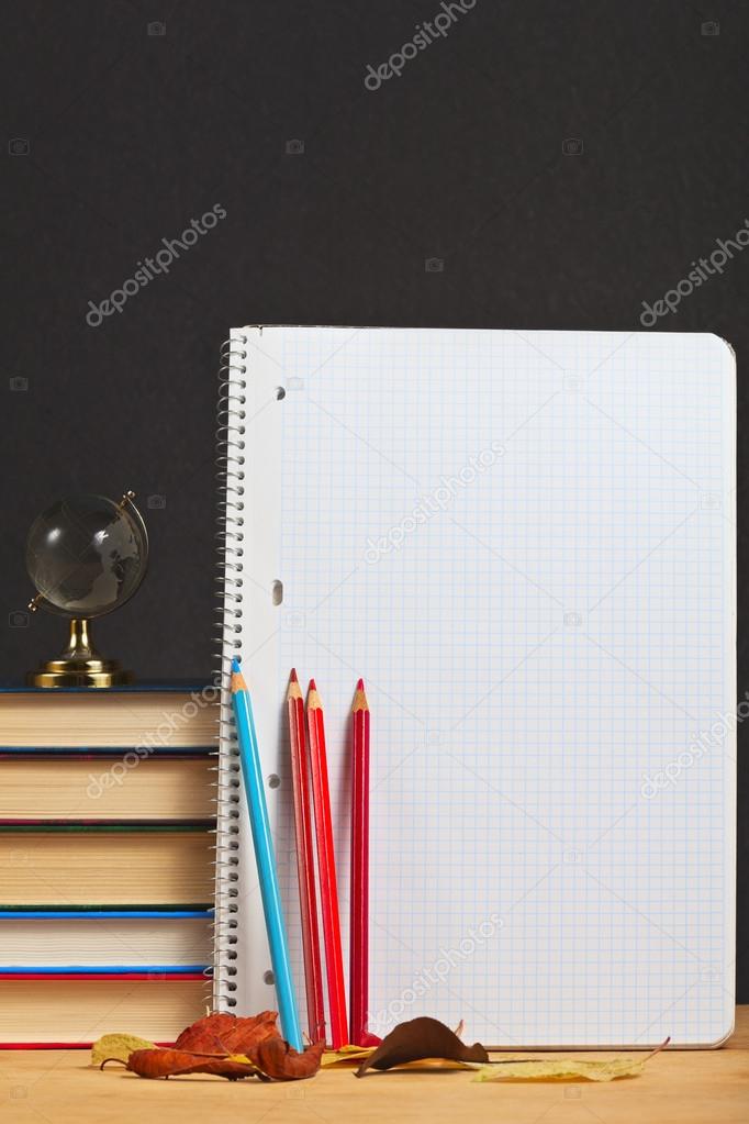 Notebook with colored pencils and globe on a wooden surface.