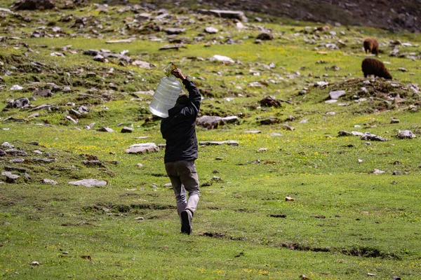 A man carrying a gallon of water while walking on a grassland