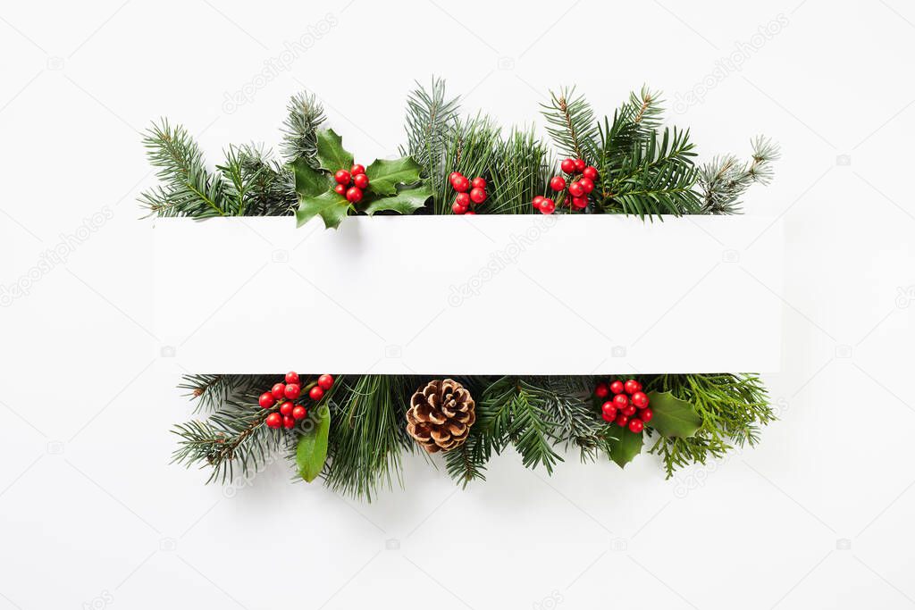 Composition of red holly berries and green fir tree branches on white background. Winter natural decoration. Botanical festive flat lay, top view.
