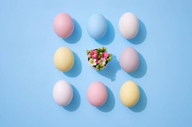 Mavi arka planda bahar çiçekleri olan renkli Paskalya yumurtaları. Düz konum, üst görünüm, kopyalama alanı.
