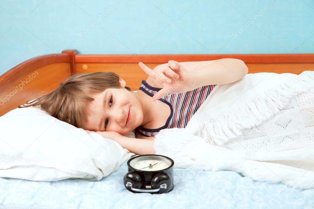 Small boy in bed with alarm clock