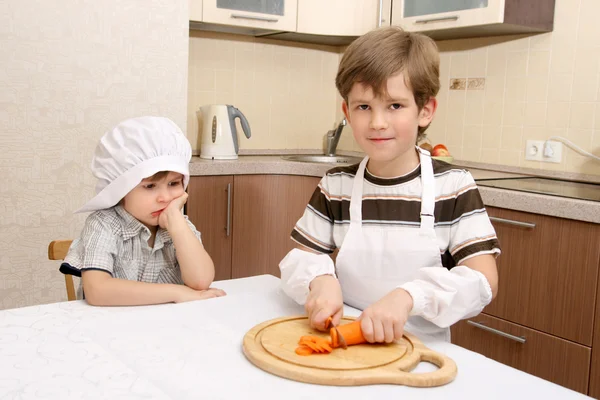 Мальчик с морковью на кухне — стоковое фото