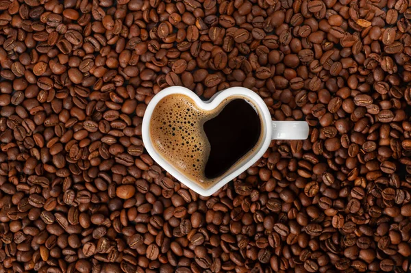 Café com uma bela espuma em uma caneca na forma de um coração em um fundo de grãos de café. espaço de cópia — Fotografia de Stock