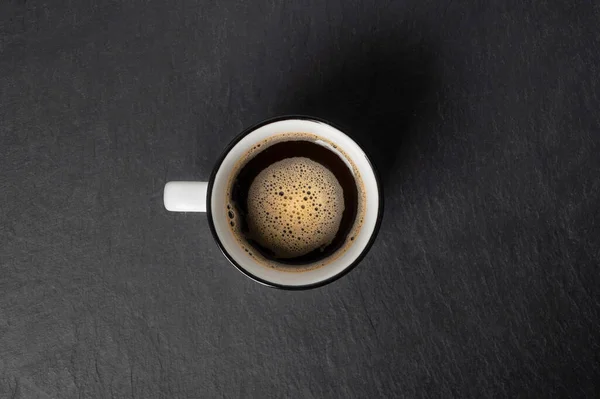 Uma xícara de café com espuma bonita perto de grãos de café são espalhados em um fundo de pedra preta espaço de cópia vista superior — Fotografia de Stock