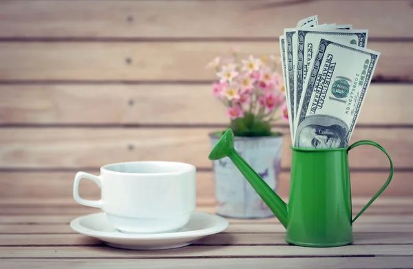 Cup of coffee and dollars in a watering can. — Stock Photo, Image