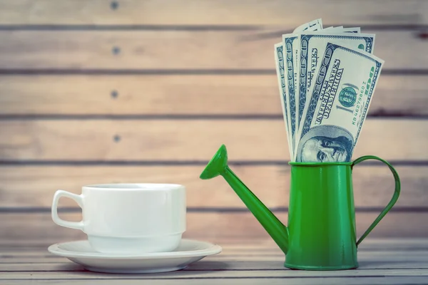 Cup of coffee and dollars in a watering can. — Stock Photo, Image