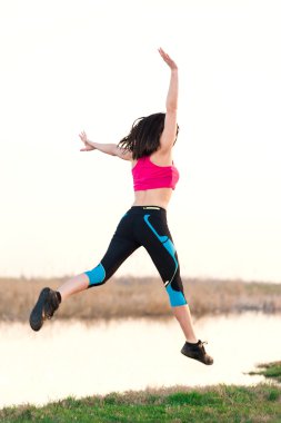 Genç spor kadın günbatımında Gölü yakınlarında havada atlama