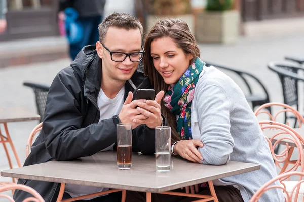 Par söker på smartphone medan du sitter på kafé tabell — Stockfoto