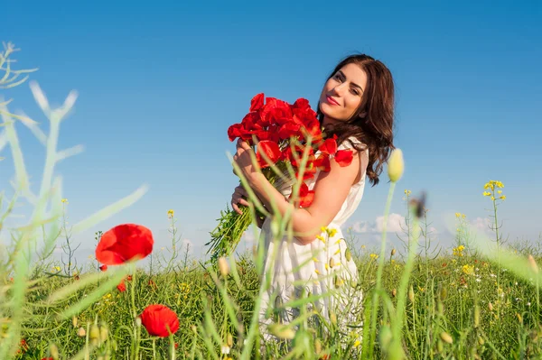 美丽的女孩，在天空和日落在田间持罂粟花花束，微笑. — 图库照片