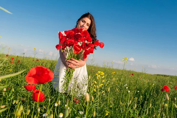 Krásná mladá žena, nebe a slunce v poli drží kytici mák, usmíval se. — Stock fotografie