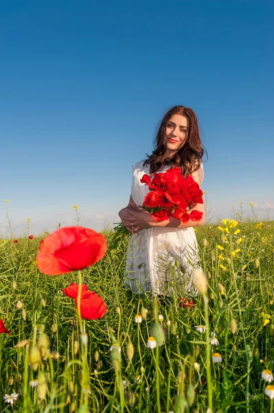 Mooie elegante vrouw over hemel en zonsondergang in het veld bedrijf een papavers boeket, glimlachend. — Stockfoto