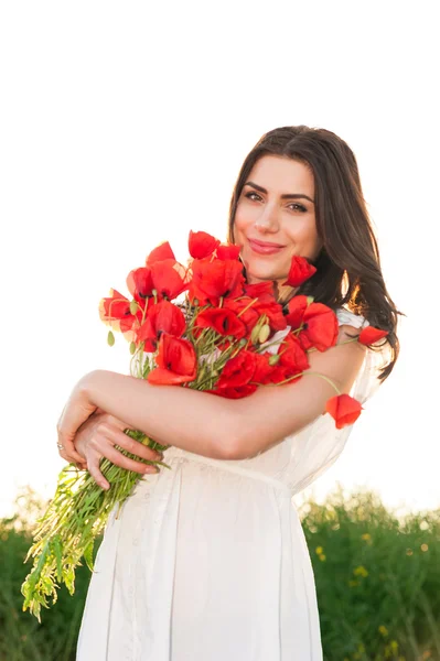 Wanita cantik di atas langit dan matahari terbenam di lapangan memegang buket bunga poppy, tersenyum — Stok Foto
