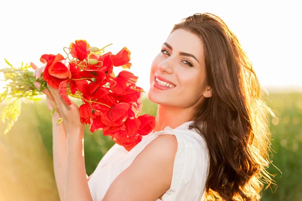 Mooi meisje over hemel en zonsondergang in het veld bedrijf een papavers boeket, glimlachend — Stockfoto