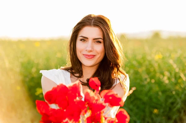 Beautiful woman over Sky and Sunset holding a poppies bouquet and smiling — Stock Photo, Image