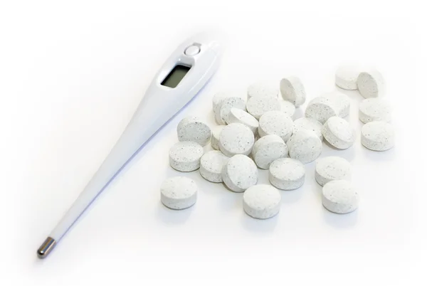 Электронный термометр и таблетки на белом фоне — стоковое фото