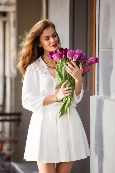 Söt flicka i vit klänning och en vacker bukett tulpaner. — Stockfoto