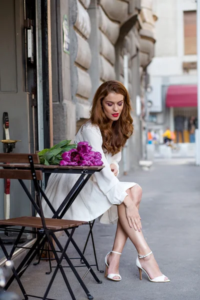 Menina bonito em vestido branco e um belo buquê de tulipas . Fotos De Bancos De Imagens