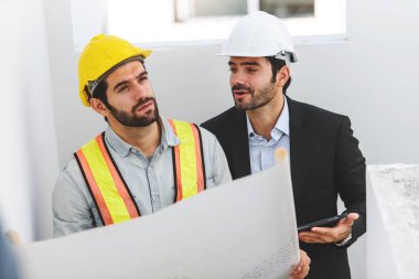 İnşaat mühendisi ve inşaat işçisi elinde dijital tablet ve planlarla inşaat alanından bahsedip duruyor. İşbirliği takım çalışması kavramı