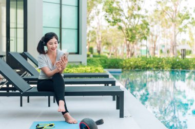 Akıllı telefon kullanan Asyalı kadın antrenmandan sonra dinleniyor.