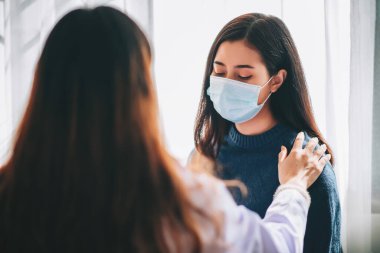 Asyalı doktor, hastanede ofis sendromu ve depresyonu olan genç bir kadını muayene ediyor. Doktor, Covid-19 salgınını korumak için maske takıyor ve sağlık hizmetlerine danışmanlık yapıyor.