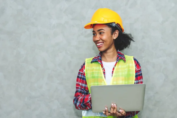 建設現場や倉庫で働くためのハード帽子の安全を身に着けているプロの若い黒人女性土木技術者 建築労働者の肖像 仕事のためのラップトップを使用して — ストック写真
