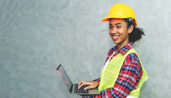 Portrait of professional young black woman civil engineer , architecture worker wearing hard hat safety for working in construction site or warehouse,using laptop for work.