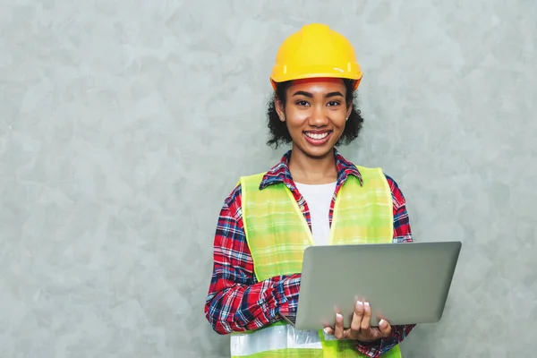 Portrait of professional young black woman civil engineer , architecture worker wearing hard hat safety for working in construction site or warehouse,using laptop for work.